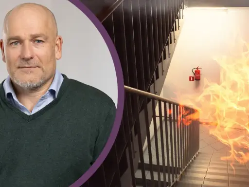 Man med skägg och en brandhärjad trappa med brandsläckare. Viktigt med revisionsbesiktning brandlarm för säkerheten.