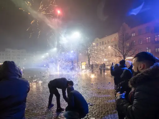 Folk ser på fyrverkerier olagligt på en stadsgata med julgran och byggnader.