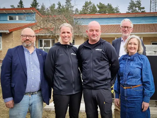 Fem personer står framför en byggnad. Två bär svarta träningsjackor med texten "GÖSAL". En man i blå kavaj och jeans, en kvinna i jeanskjol och en man i kostym. Kanske diskuterar de sotningskurs pris.