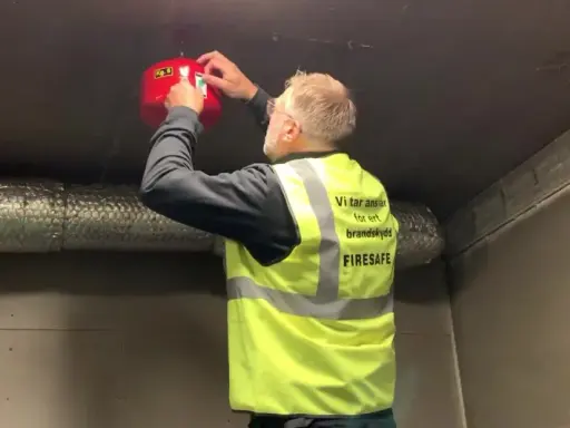 Man i varselväst installerar en brandsläckare i ett utomhus soprum.