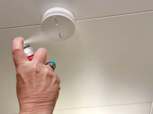 En hand sprayar en uppkopplad brandvarnare i taket.