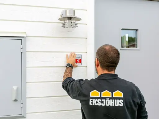 Man monterar en Verisure-larmdekal på husfasaden, en del av ett smart hem-system som kan integreras med Google Home.