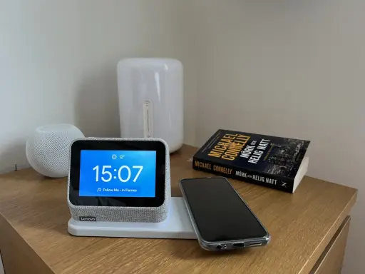 En smartklocka visar 15:07, en mobil ligger redo att ladda mobilen på natten bredvid en bok.