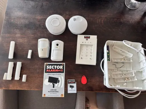 Säkerhetssystem från Sector Alarm, inklusive larmpanel, rörelsedetektorer, dörrsensorer och en tom larmcentral. Perfekt för en trygg home assistant.