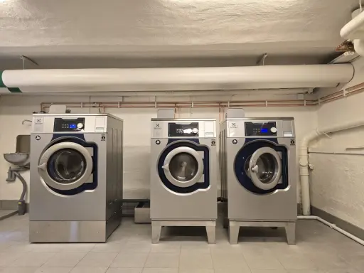 Tre professionella torktumlare i metall. En varningssymbol för torktumlare brandrisk syns på en av maskinerna.