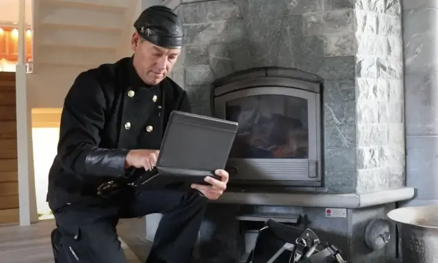 Sotare med laptop vid eldstad. Regelbunden brandskyddskontroll hur ofta är viktig för säkerheten.