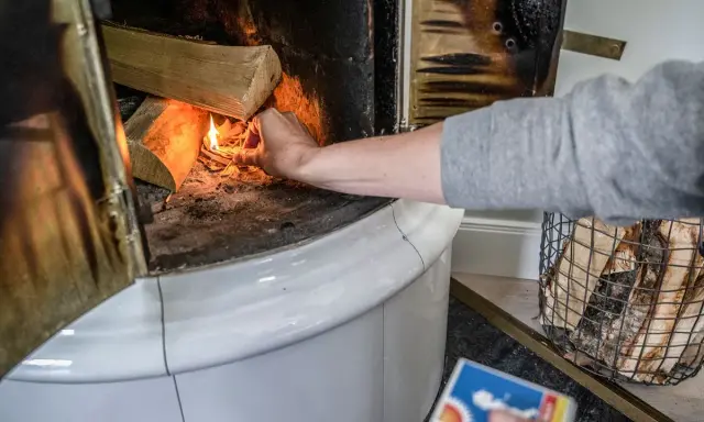 En hand tänder eld i en kakelugn med vedträn som väntar på att värmas.