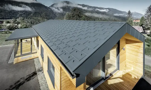 Modernt hus med grått plåttak, där åskledare diskret integrerats. Omgivet av berg och skog.