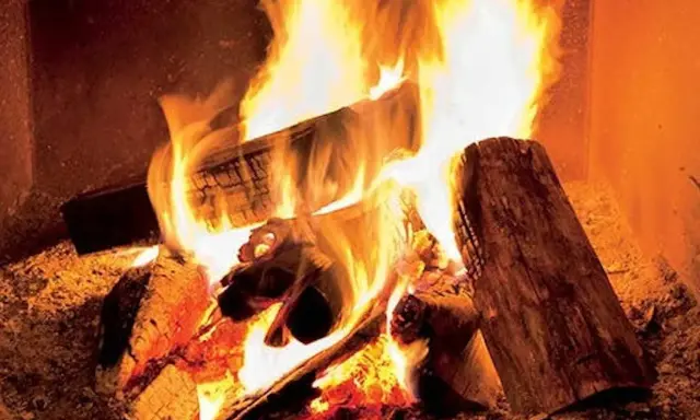 Eldar med tallved i en sprakande brasa. Värmen sprider sig från de glödande stockarna.