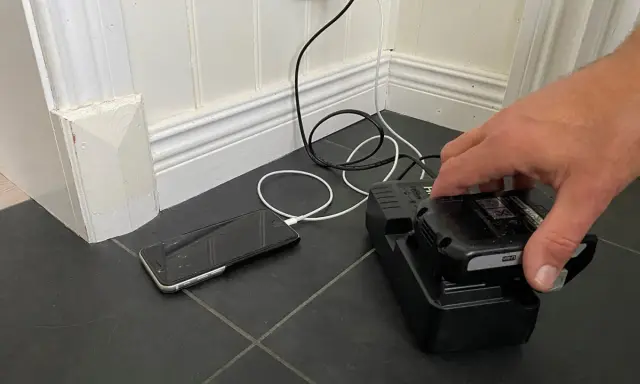 En hand placerar ett litiumbatteri på en laddare. En mobiltelefon laddas bredvid.