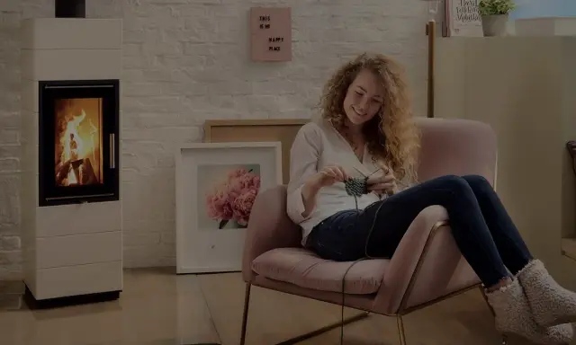 En kvinna stickar i en mysig fåtölj bredvid en sprakande kamin. Frågan är hur varmt blir det i en kamin?
