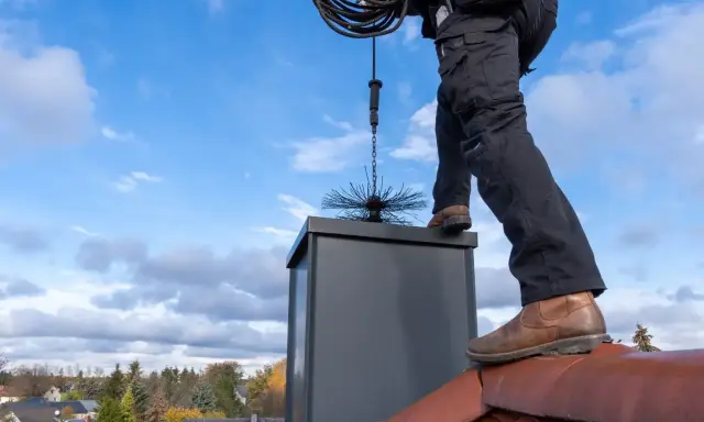 Sotare på taket med verktyg för sotning. En brandskyddskontroll pris kan variera beroende på skorstenens skick.