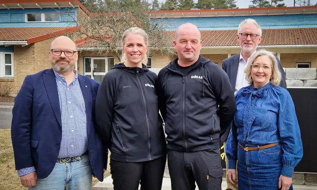 Fem personer står framför en byggnad. Två bär svarta träningsjackor med texten "GÖSAL". En man i blå kavaj och jeans, en kvinna i jeanskjol och en man i kostym. Kanske diskuterar de sotningskurs pris.