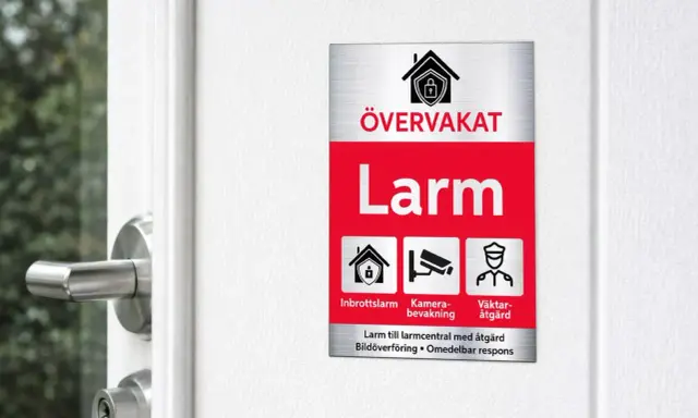 En larmskylt utan larm, men med symboler för inbrottslarm, kameraövervakning och väktaråtgärd, sitter på en vit dörr.