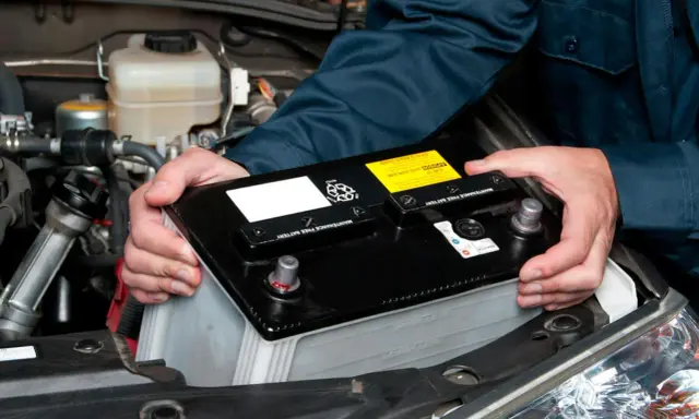 Mekaniker byter bilbatteri. Undvik kortslutning bilbatteri genom att hantera det varsamt.