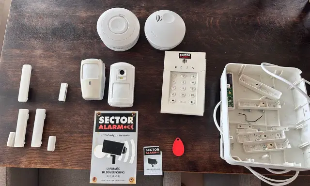 Säkerhetssystem från Sector Alarm, inklusive larmpanel, rörelsedetektorer, dörrsensorer och en tom larmcentral. Perfekt för en trygg home assistant.