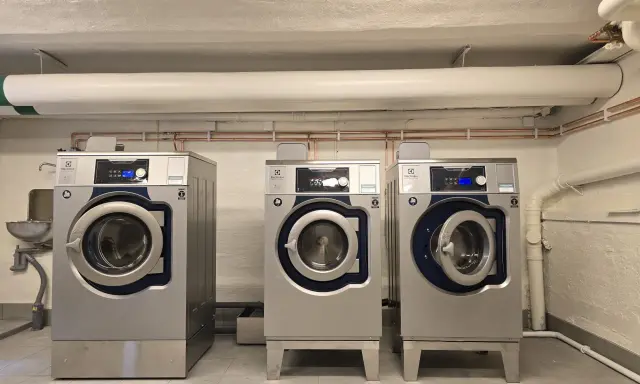 Tre professionella torktumlare i metall. En varningssymbol för torktumlare brandrisk syns på en av maskinerna.