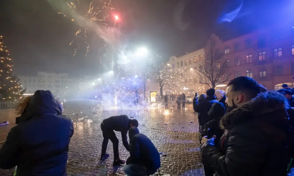 Folk ser på fyrverkerier olagligt på en stadsgata med julgran och byggnader.