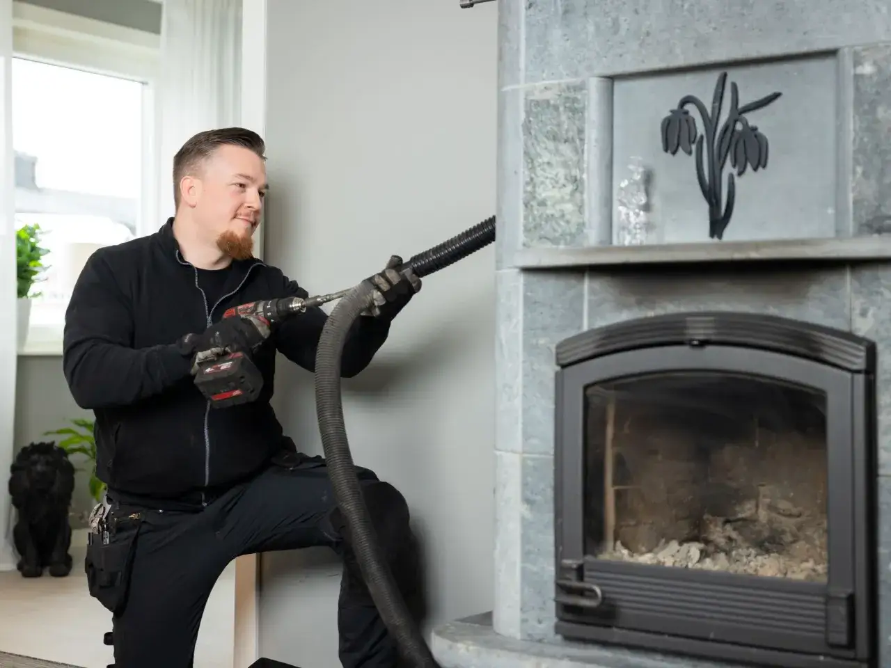 En sotare anv&auml;nder en borrmaskin och slang f&ouml;r att reng&ouml;ra en eldstad. Han visar hur sotar man effektivt f&ouml;r att undvika brandrisker.