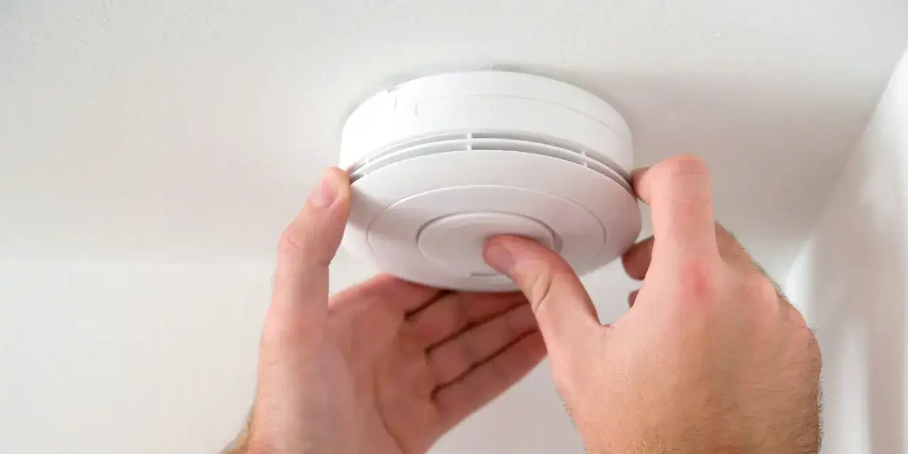 Händer monterar en vit brandvarnare, en Google Nest Protect, i taket.