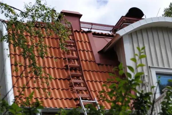 Takstege på ett rött tegeltak, en del av taket syns genom lövverk. Kanske för att följa takstege regler vid sotning.