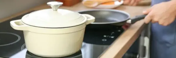 En person lagar mat på en induktionshäll med en kastrull och en stekpanna. En spisvakt kan förhindra olyckor genom att övervaka värmen.