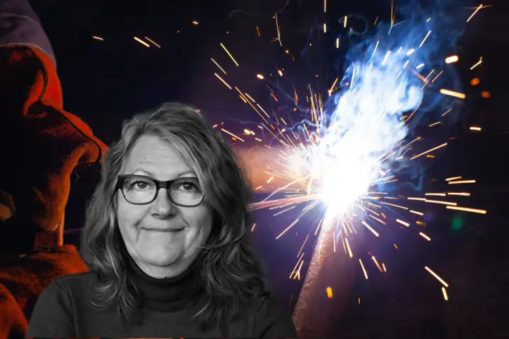 Kvinna med glasögon ler framför en bakgrund av gnistor från heta arbeten. En svetsare i skyddskläder syns till vänster.