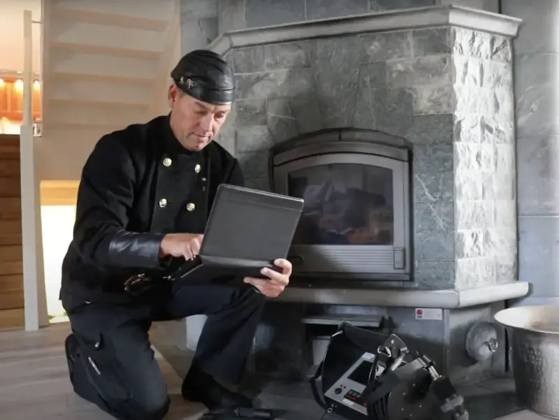 Sotare med laptop vid eldstad. Regelbunden brandskyddskontroll hur ofta är viktig för säkerheten.